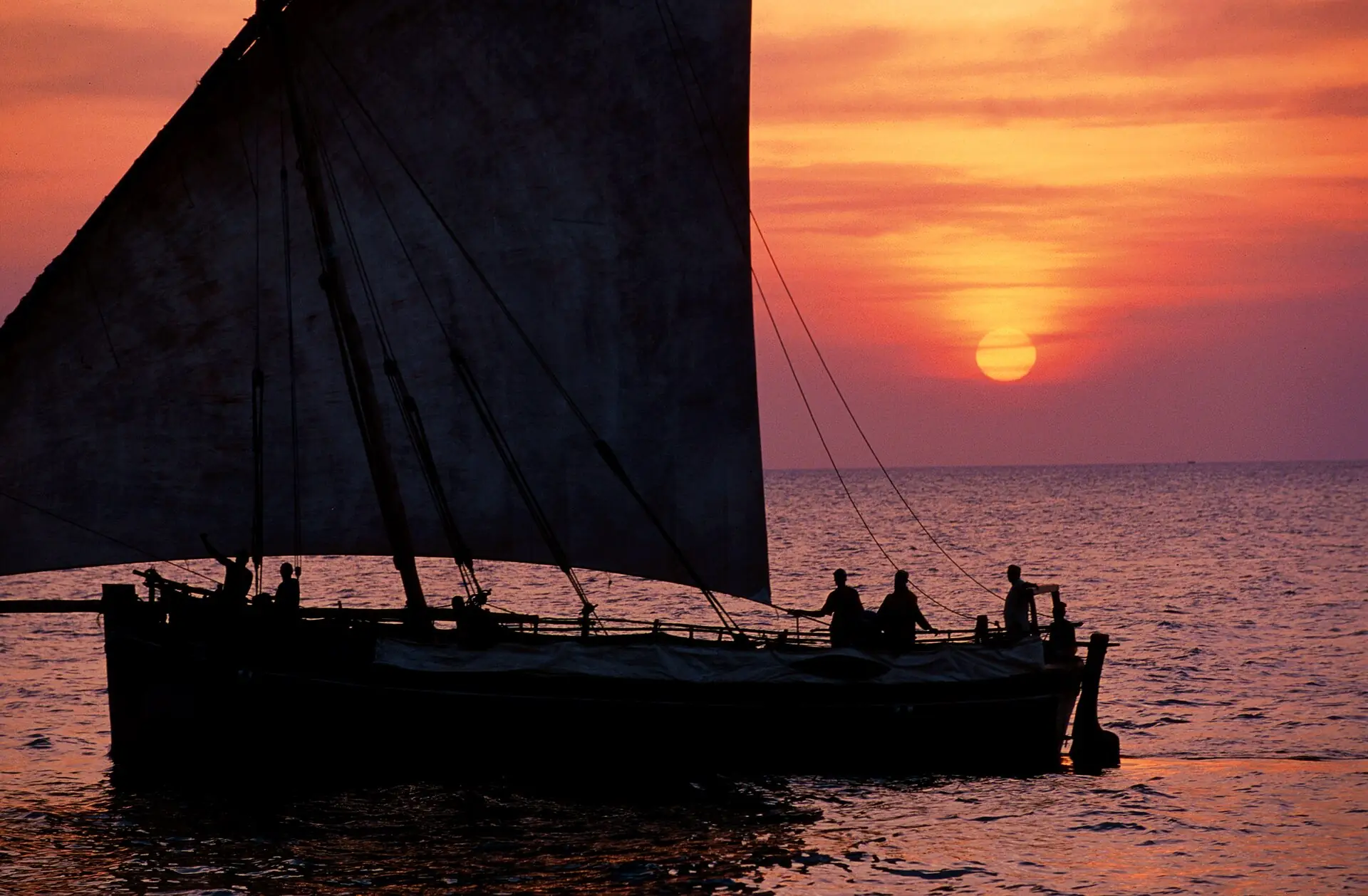 A wooden dhow sailing at sunset off Zanzibar